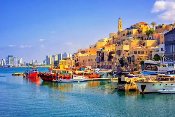 Bunte Boote im Hafen von Tel Aviv, mit der historischen Altstadt im Hintergrund und modernen Hochhäusern am Horizont.